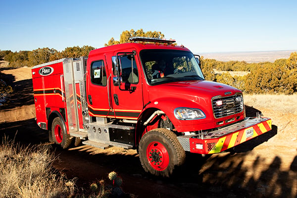 Officer’s side of a Pierce BX™ Wildland Fire Truck parked outside near trees on a sunny day. 