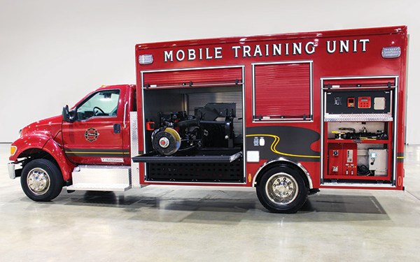 Pierce Mobil Training vehicle parked inside with its driver’s side compartment doors open showing storage space. 