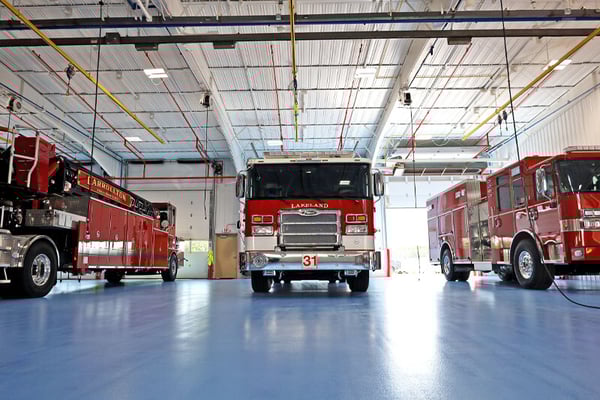 Three fire trucks are parked side-by-side inside Pierce Manufacturing’s facility in Appleton, WI, on the blue floor. 