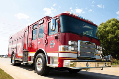 A red Pierce stock truck driving down the road with a blue sky and green tree in the background.