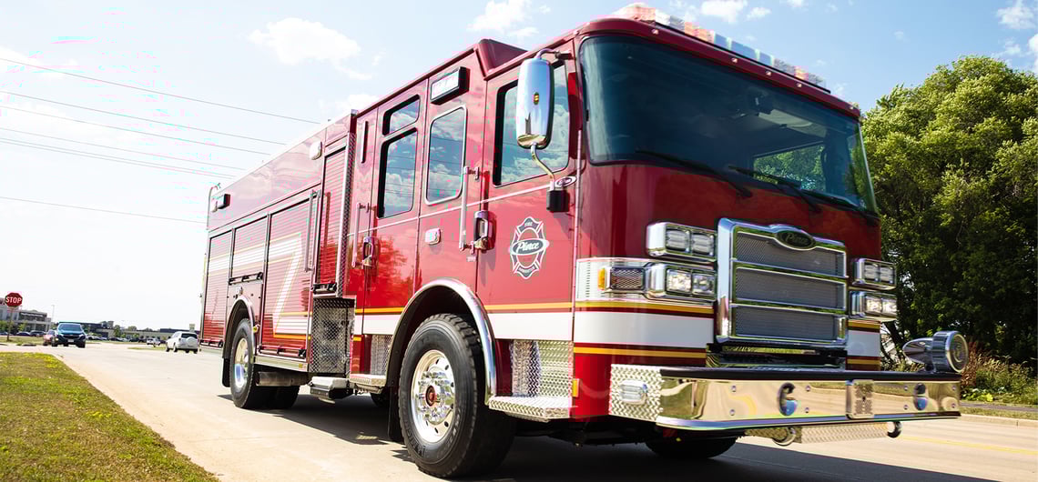 A red fire truck on pavement with blue sky and green trees in the background.