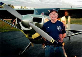 A man named Bill standing in front of a prop plane.