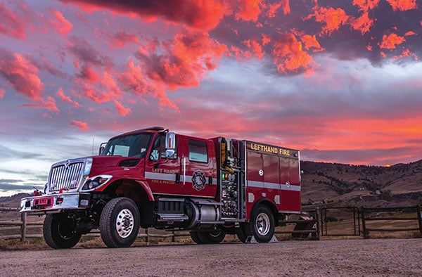 Pierce Wildland Fire Truck parked outside in the dessert near a fence while the sun is setting.