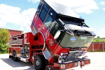 A red and black pumper apparatus is parked with the cab lifted. 