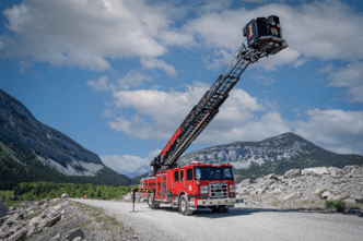 A red aerial fire truck with black ladder extended in a mountainous region.