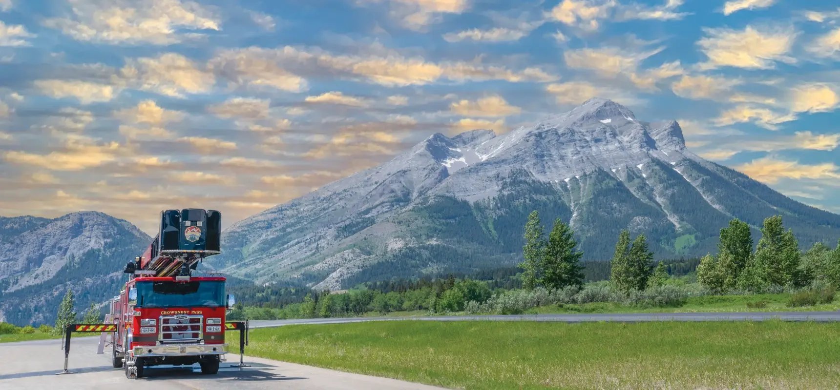 Red Pierce aerial fire truck with stabilizers deployed in front of a rugged mountain peak.