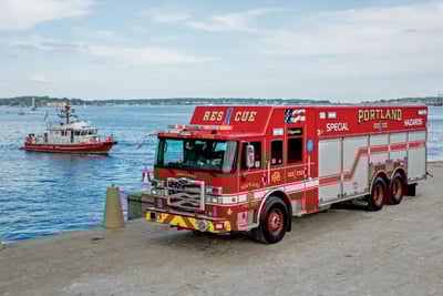 A Portland Maine Fire Department Special Hazards rescue truck parked next to a fire boat on a coastal pier.