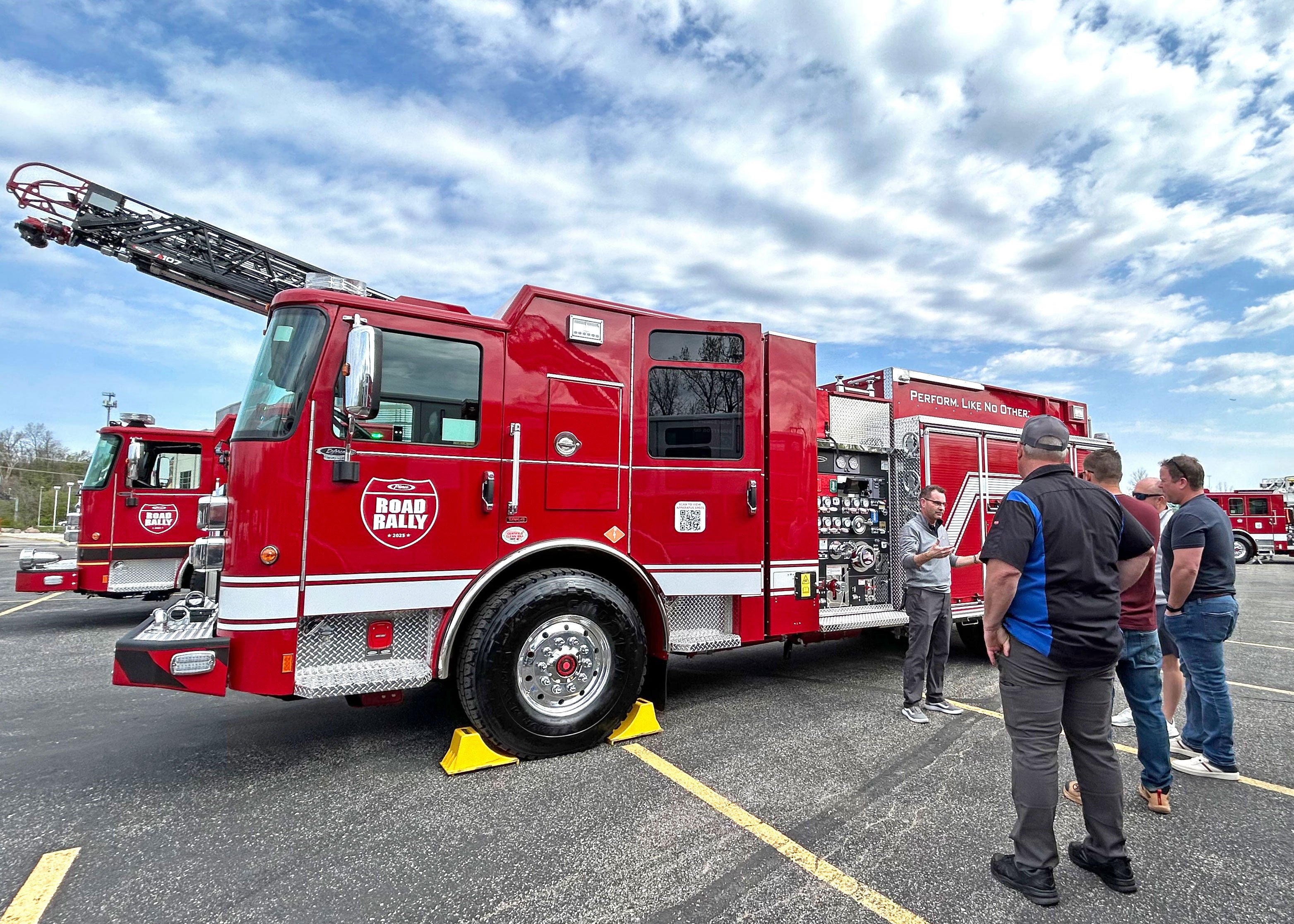 Firefighters looking at a Pierce Volterra Electric Fire Truck on a sunny day.