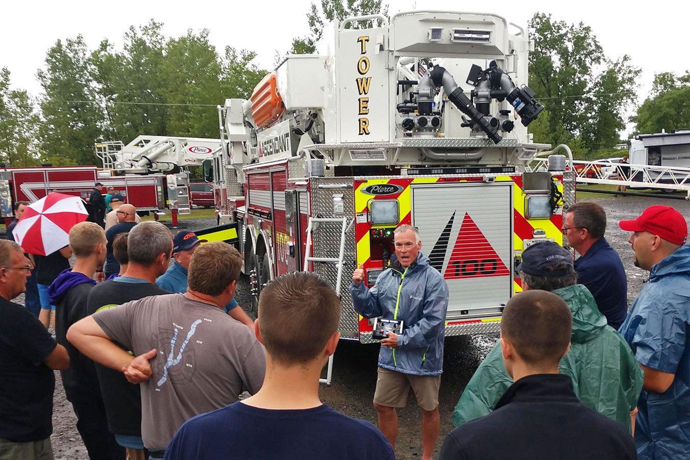 A man surrounded by a group of people standing next to a Pierce Fire Truck giving a demonstration outside at a Pierce Road Rally Event.