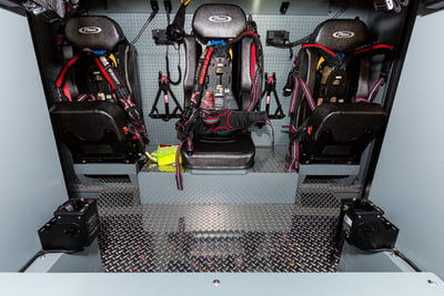 Three black fire truck seats with red and black seatbelts.