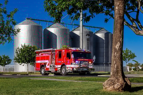 The front officers side of a Velocity Volterra Electric Vehicle parked in front of silos on a sunny day.