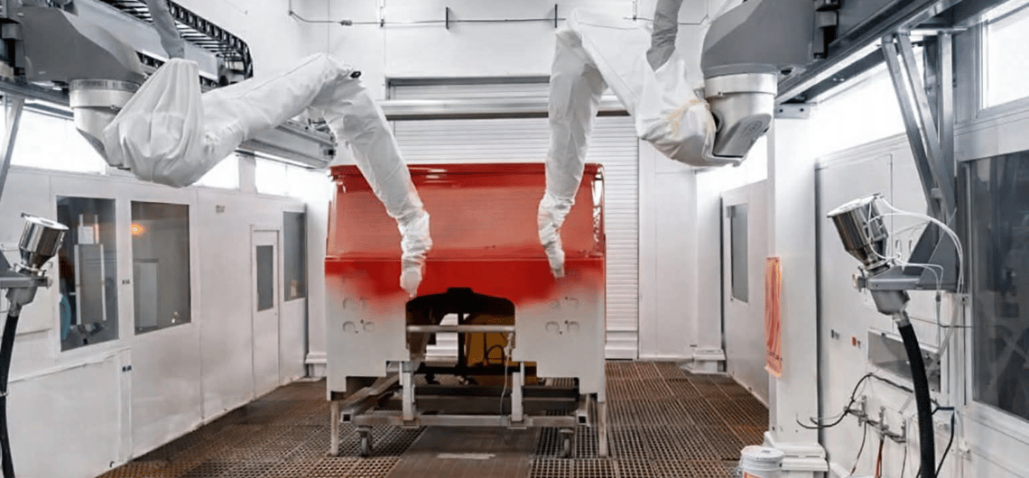 Automated robotic arms applying paint to a red fire truck cab in a professional paint booth.
