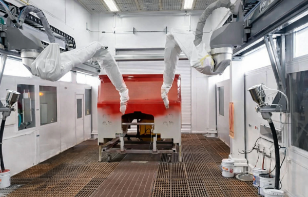 Automated robotic arms applying paint to a red fire truck cab in a professional paint booth.