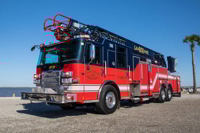 The front drivers side of an Enforcer Ascendant 107 Aerial Ladder fire truck parked beside the ocean and palm trees.