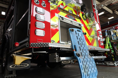 The rear of a fire truck at a service shop with a crawler leaning against it.