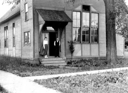 Humphrey Pierce standing beside a woman in the doorway on the front steps of the first Pierce Manufacturing building. 