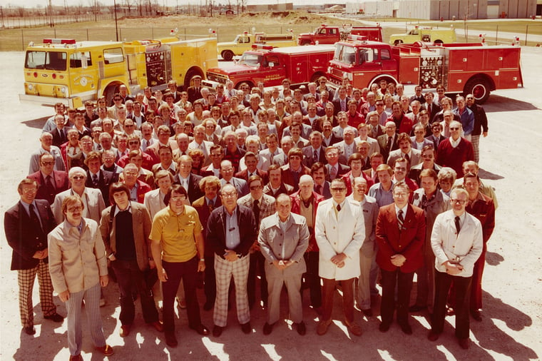 Group photo of Pierce Manufacturing employees standing outside near firetrucks. 