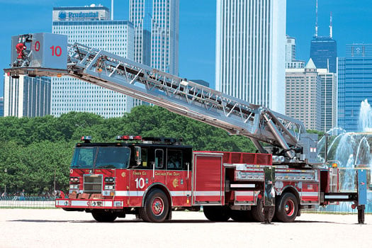 Pierce 100-foot Aerial platform fire apparatus parked outside near a water fountain surrounded by skyscrapers. 