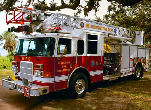 Pierce Manufacturing 75’ Aerial Ladder parked outside on the grass surrounded by trees. 