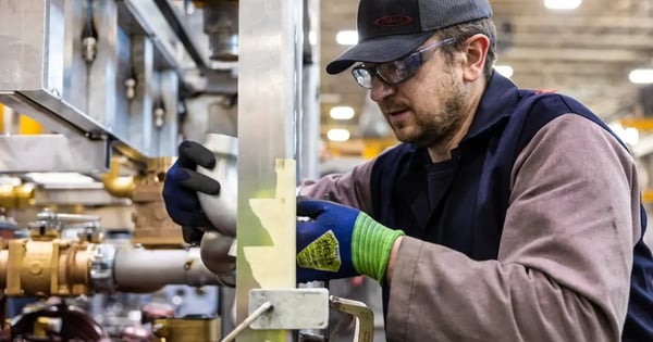 A Pierce Manufacturing worker wearing safety gear assembles custom metal piping on a fire truck chassis.