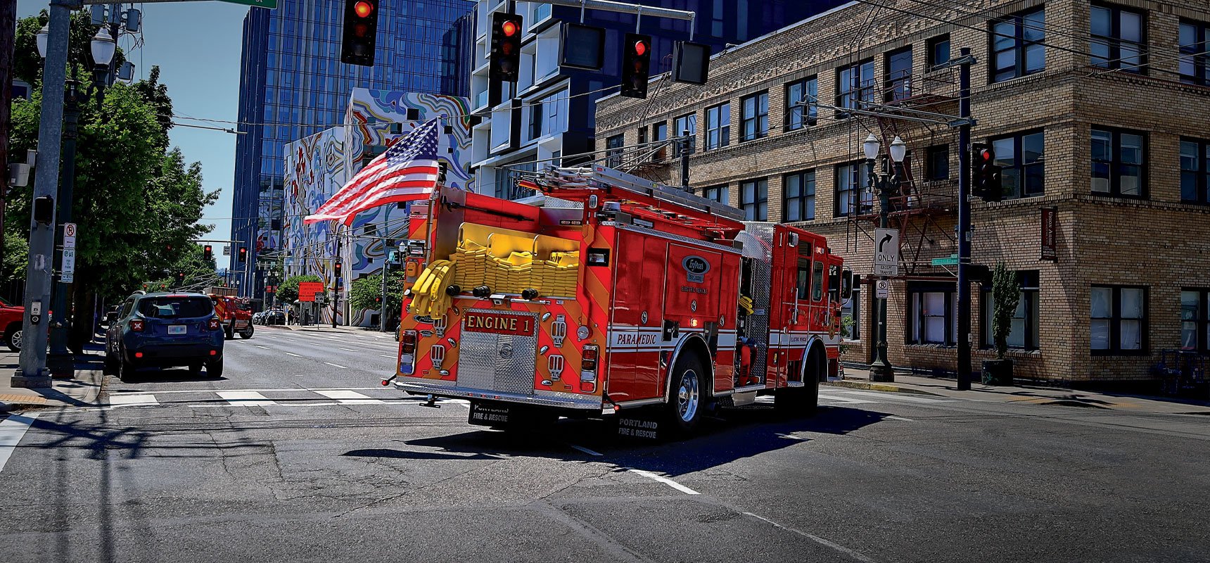 A red high voltage electric fire truck turns a corner at a city intersection.  