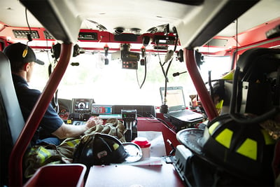 An interior image of an electric fire truck cab shows the front windshield, driver and passenger going about day-to-day operations. 