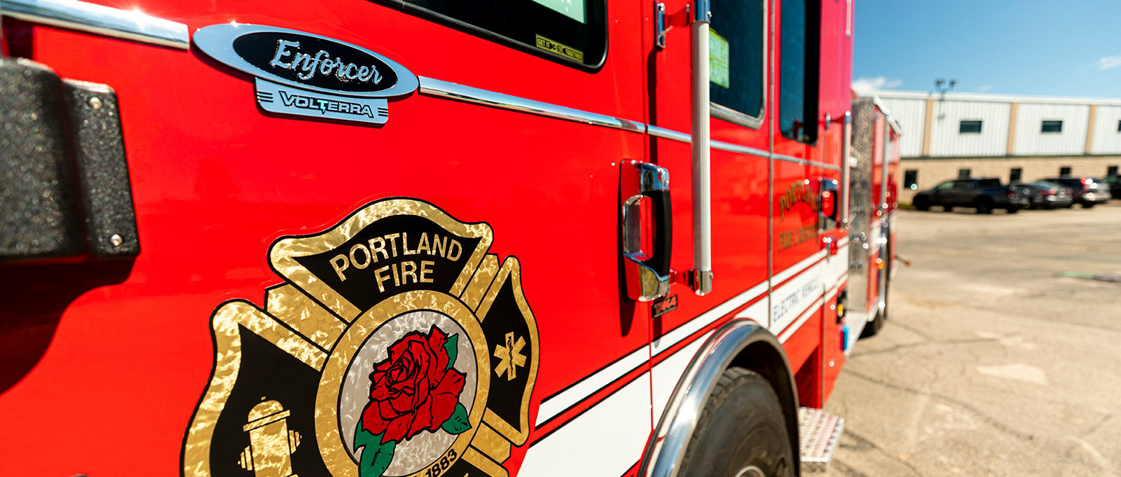 A close-up image shows the diver side panel of the Portland Fire Rescue electric fire truck with the emblem. 