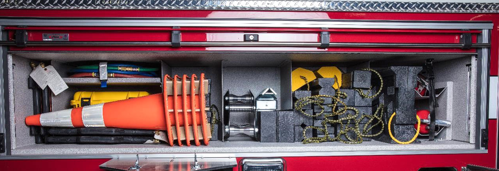 An open compartment of an aerial fire truck shows traffic cones and fire truck wheel chocks which are essential items to secure the area around the apparatus on-scene. 