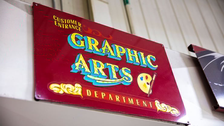 A metal red sign for the graphic arts department above a doorway. 