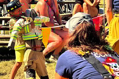 A young kid participating in a junior firefighters challenge carries a dummy during his training