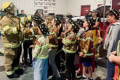 A group of kids who are Junior Firefighters in Training stand looking up to a firefighter.