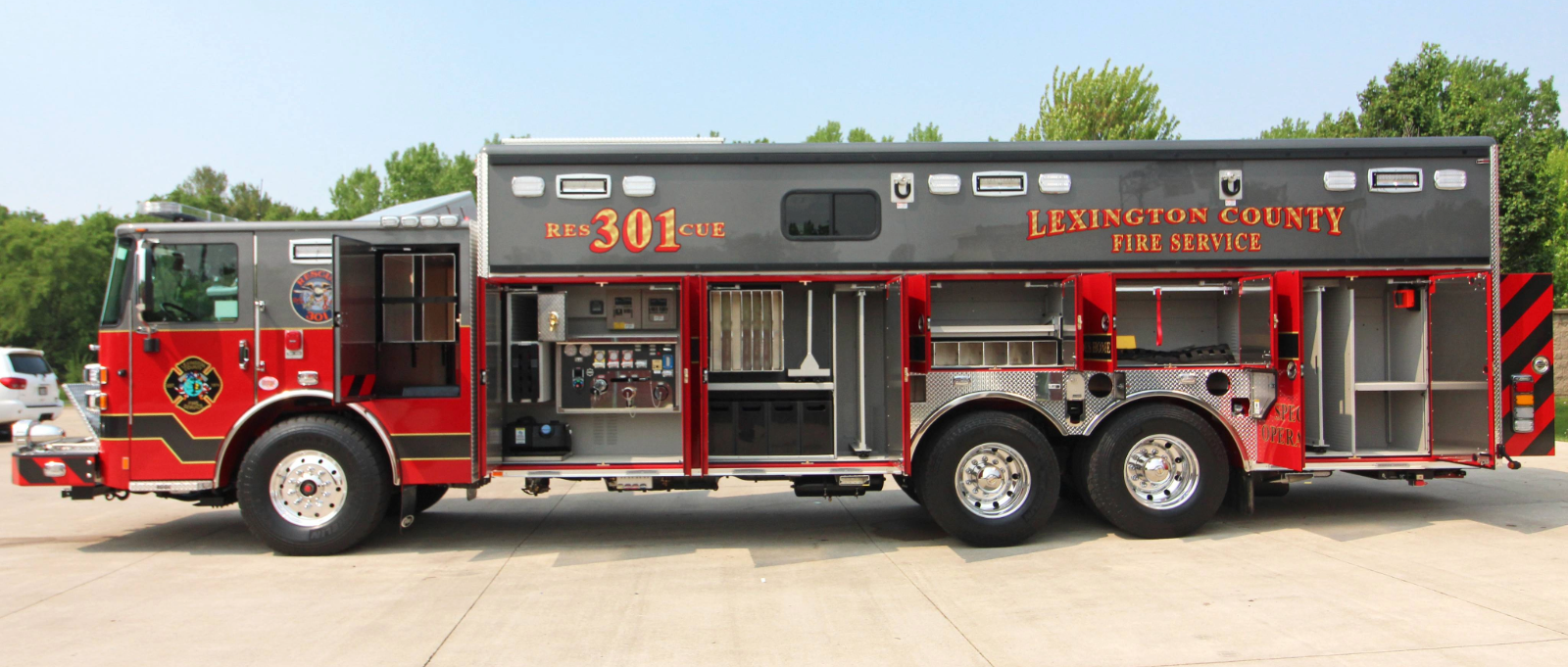 A side view of the Lexington County Fire Service rescue truck sitting on pavement with green trees and a blue sky in the background. 