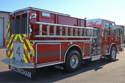 A rear side angle view of a red fire truck with a ladder hanging on the side.