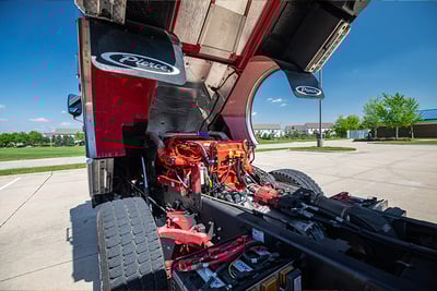 A red Pierce fire apparatus is parked in a lot with the cab tilled to show the engine and components.