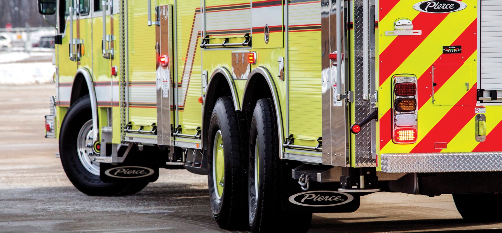 The drive side of a yellow fire truck can be seen on an asphalt road.