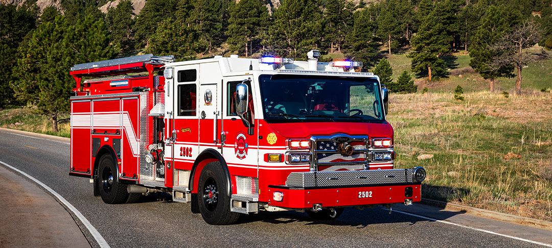 Pierce Velocity Pumper parked on a paved road surrounded by mountains, green grass and trees.