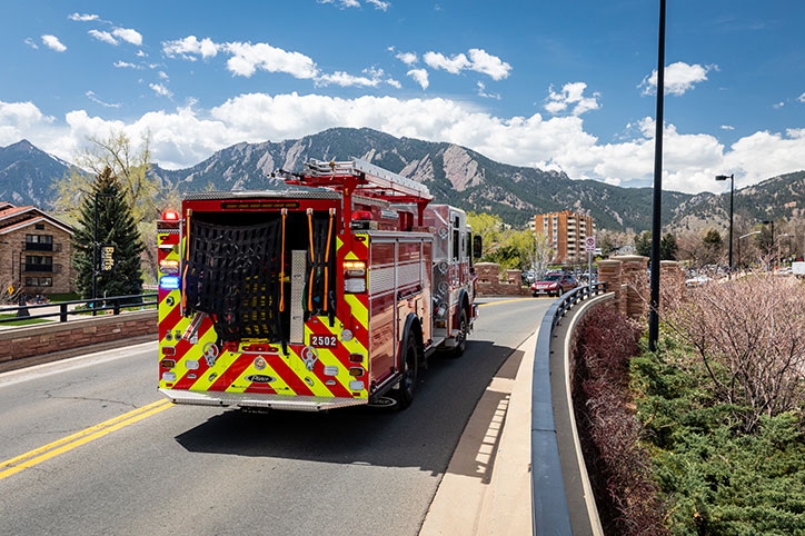 A Pierce fire truck driving over a bridge towards mountains.