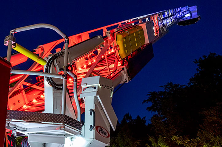 A Pierce Aerial Platform extended at night displaying red, white and blue rung aerial ladder lights.
