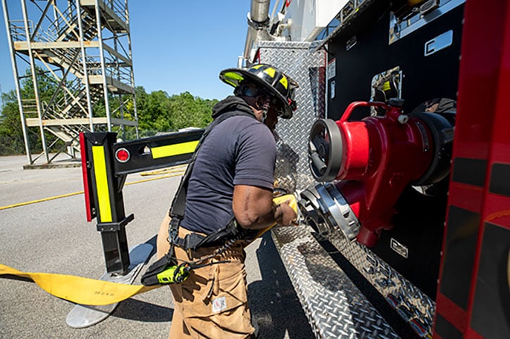 A firefighter attaching a fire hose to a fire truck.