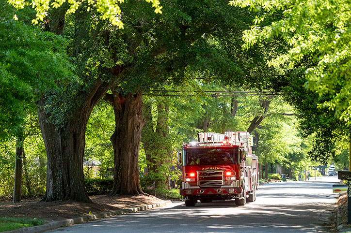 An Enforcer 100 Heavy Duty Aerial MidMount Tower driving down a road with its emergency lights on under green trees.