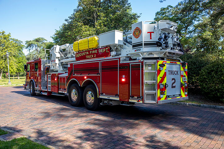 The drivers side rear of an Enforcer 100 Heavy Duty Aerial MidMount Tower driving down the road with its lights on.