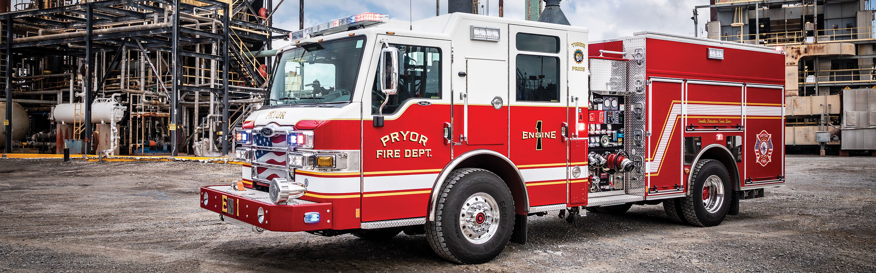 A Velocity Pumper with the lights on parked in front of an industrial plant on a cloudy day.