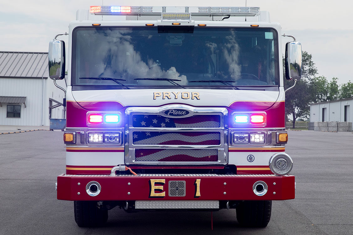 The front of a fire truck with the lights on in an empty parking lot on a cloudy day.