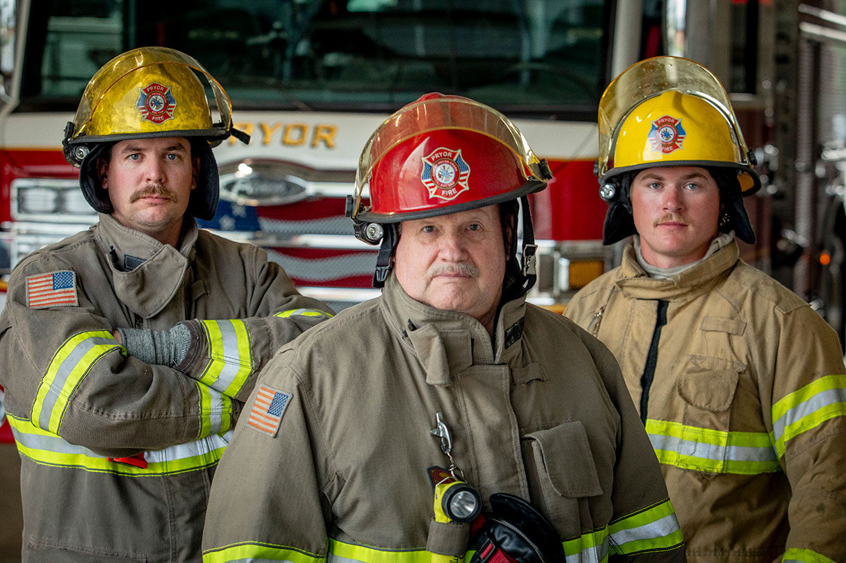 Three firefighters in turnout gear standing in front of a fire truck.