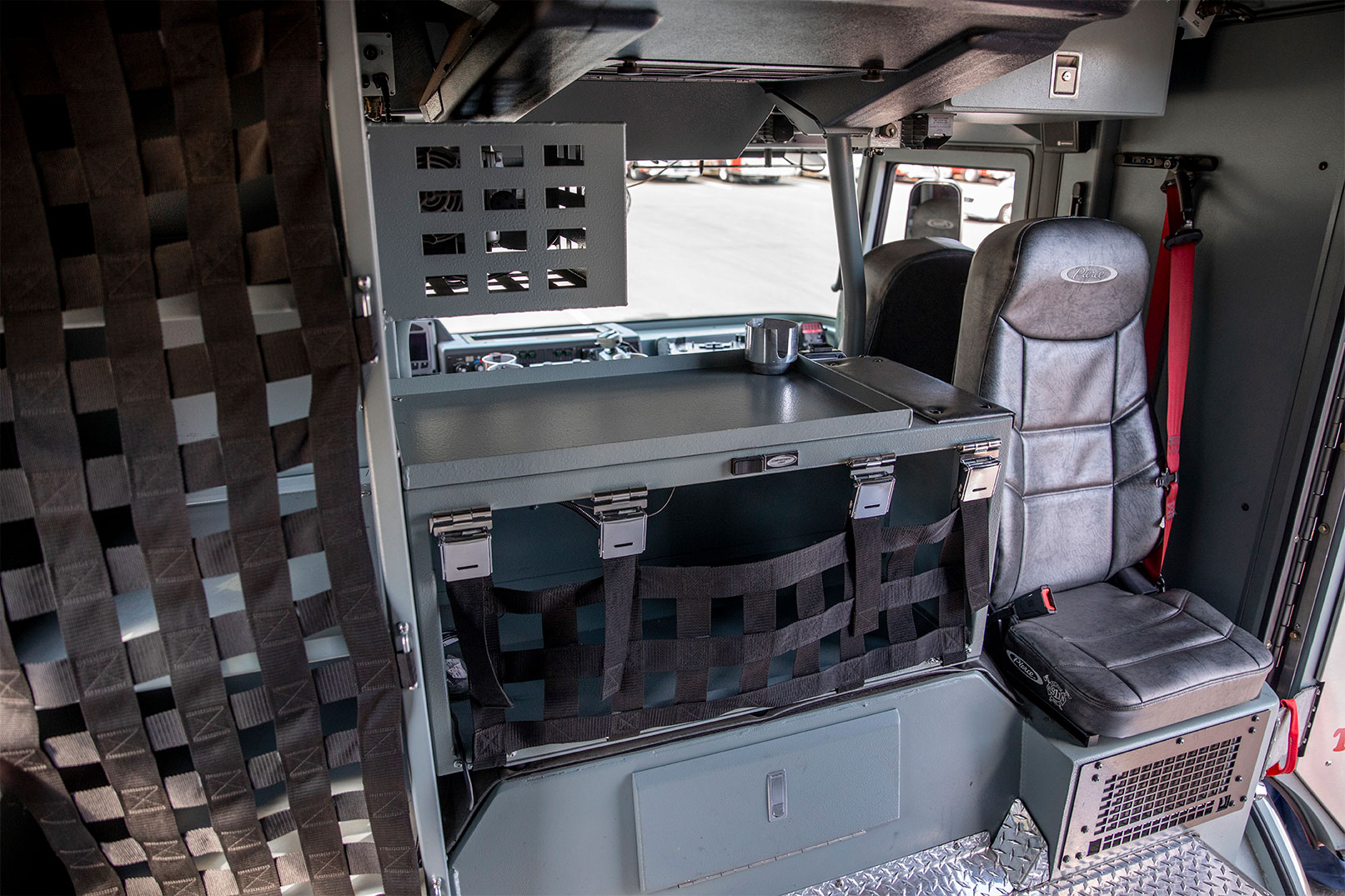 The crew cab of a fire truck with compartments with netting and a rear facing seat for a firefighter.