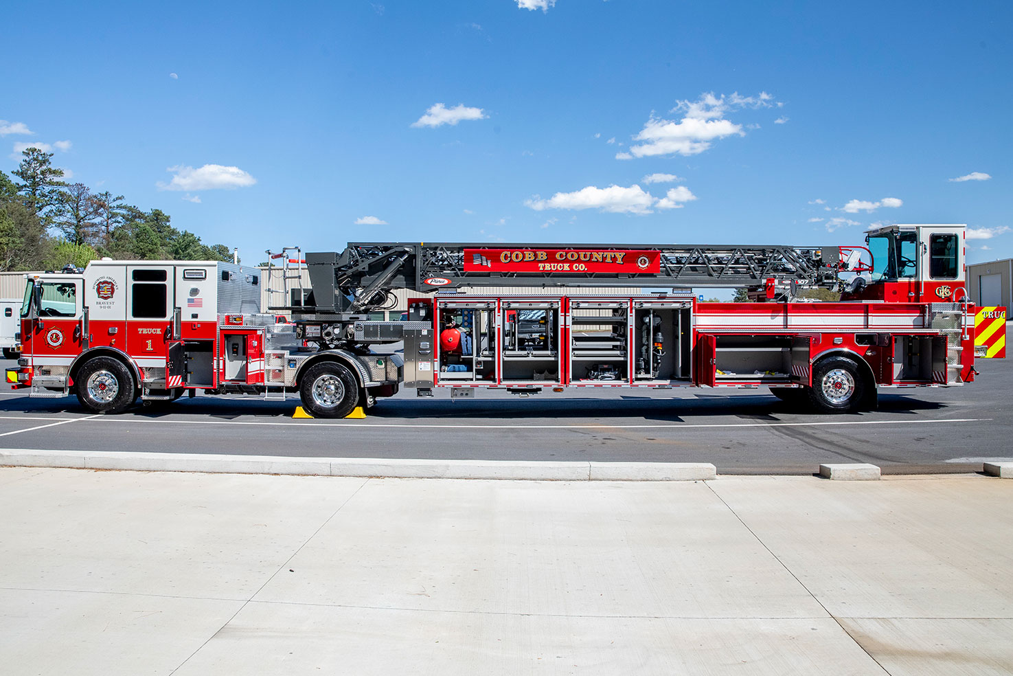 The drivers side of a tractor drawn aerial in a parking lot with the compartments open showing equipment.