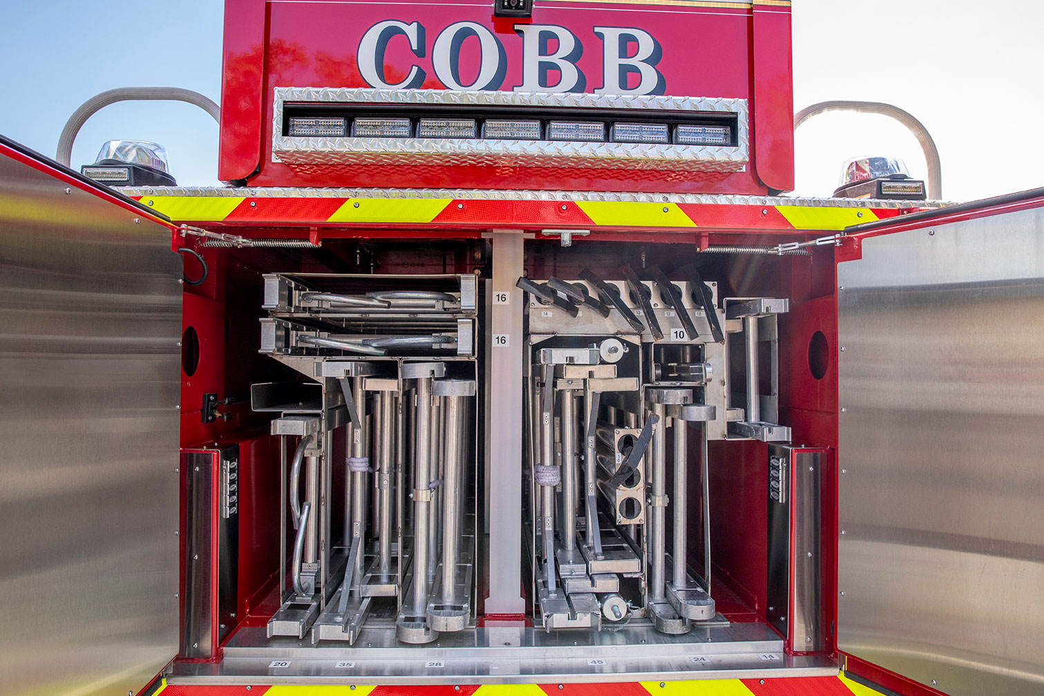 The rear of a tractor drawn aerial with the compartment open showing ground ladders and pike pole storage.