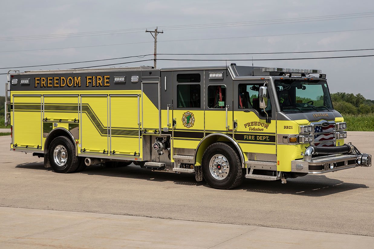 The officer's side of a yellow fire truck parked on concrete on a cloudy day.