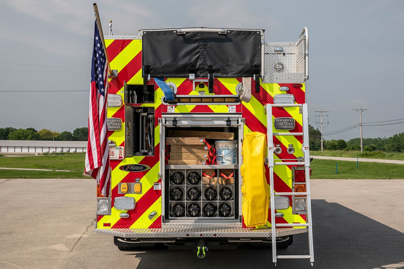 The rear of a fire truck with the compartments open showing SCBA bottles, ground ladders, cribbing and other equipment.