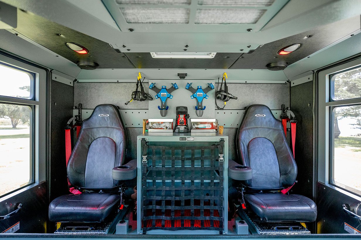 The crew cab of a fire truck with two seats, headsets and a compartment in the middle with a net cover.